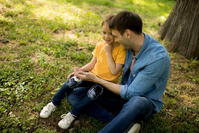Single father sitting on grass by the tree with little daughter
